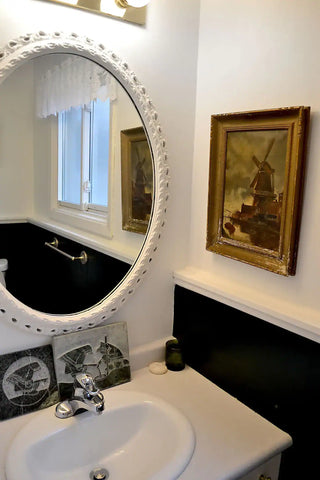 The Chic Restroom, a powder room in Cellar House NOTL, featuring an elegant interior with a vintage gold-framed painting positioned beside a stylish sink and mirror.